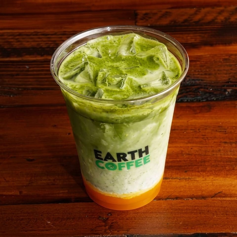 Iced green matcha latte with orange layer in an Earth Coffee cup on a rustic wooden table.